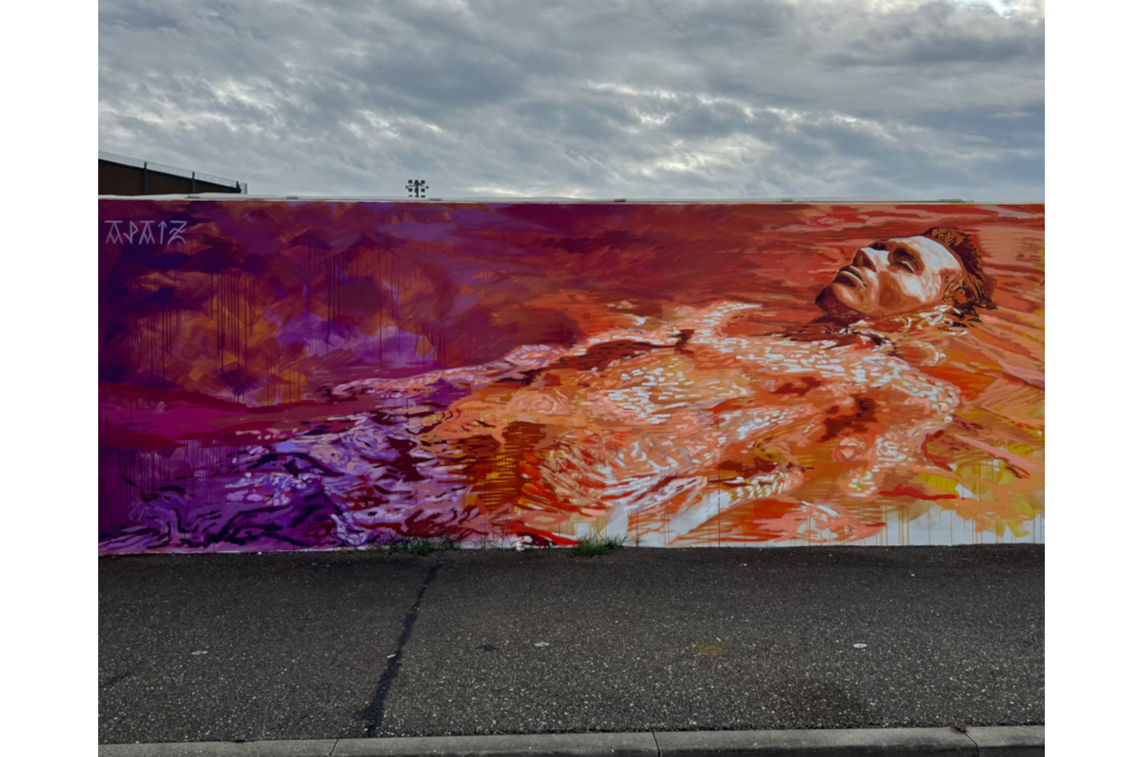 Fresque murale qui représente un homme allongé qui flotte dans l'eau dans des couleurs oranges et violettes.