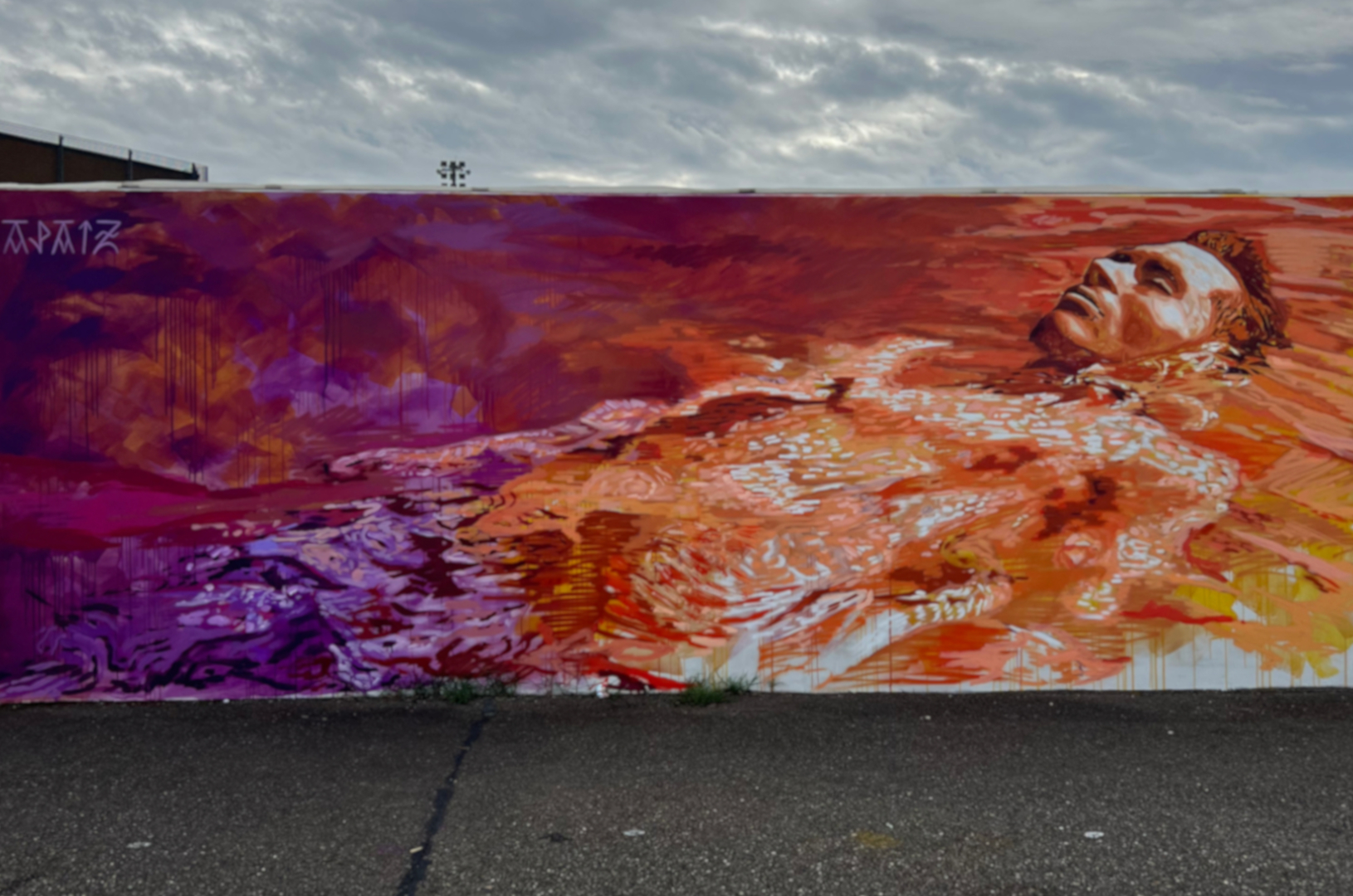 Fresque murale qui représente un homme allongé qui flotte dans l'eau dans des couleurs oranges et violettes.
