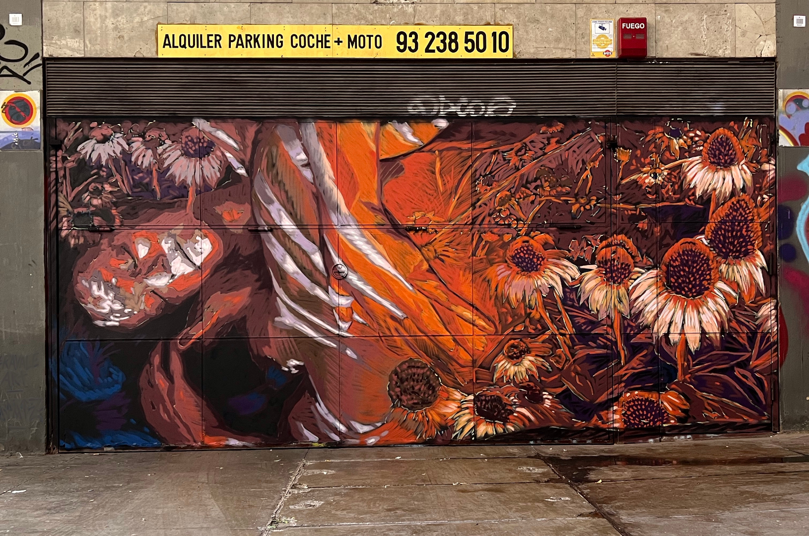 Fresque murale à Barcelone qui représente deux corps enlacés avec des fleurs autour dans des couleurs orange et bleu.