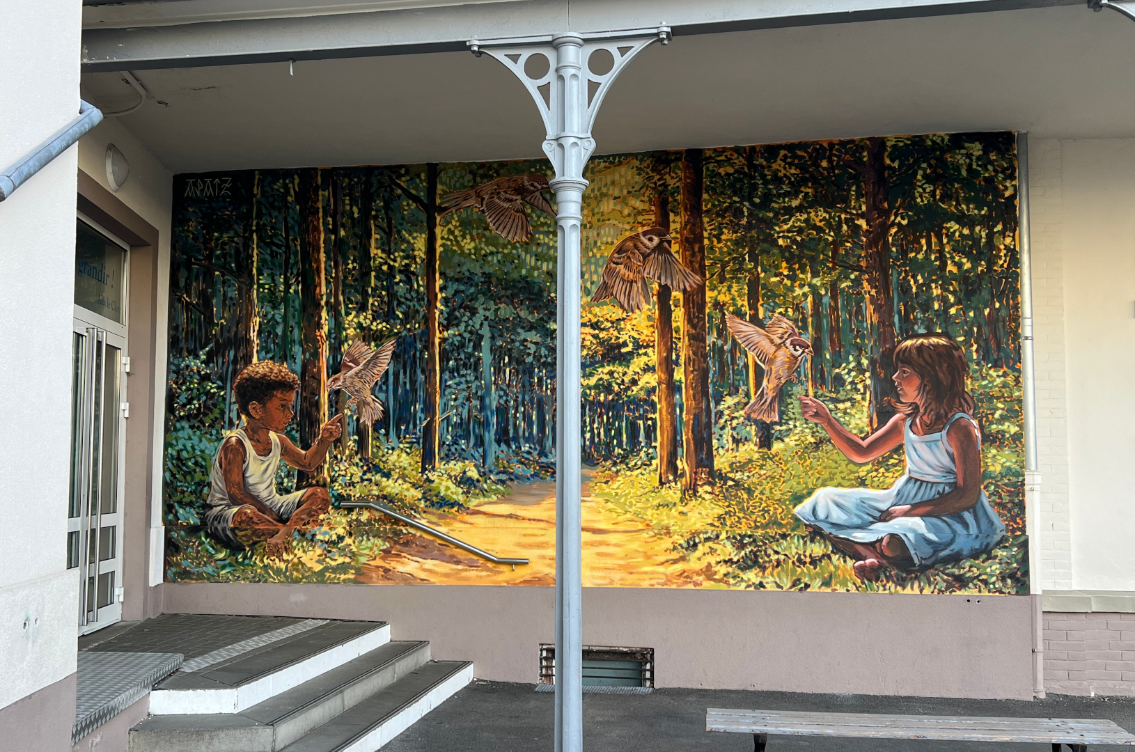 Fresque murale réalisée dans la cour de récréation de l'école Institution Notre-Dame de Strasbourg. Elle représente deux enfants qui jouent avec des oiseaux dans une forêt imaginaire.