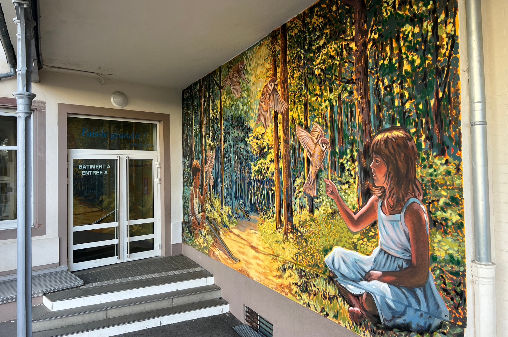 Fresque murale réalisée dans la cour de récréation de l'école Institution Notre-Dame de Strasbourg. Elle représente deux enfants qui jouent avec des oiseaux dans une forêt imaginaire.