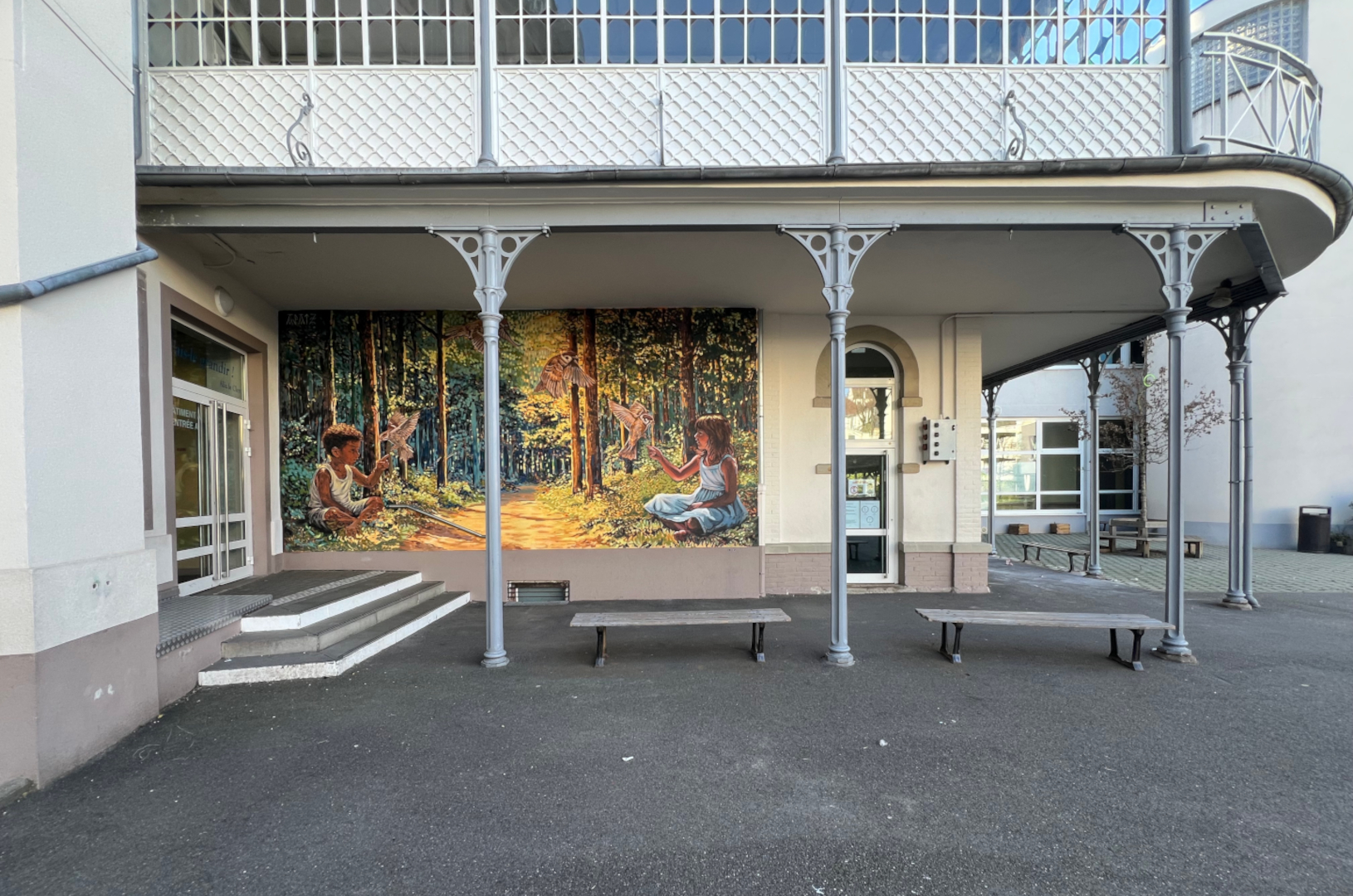 Fresque murale réalisée dans la cour de récréation de l'école Institution Notre-Dame de Strasbourg. Elle représente deux enfants qui jouent avec des oiseaux dans une forêt imaginaire.