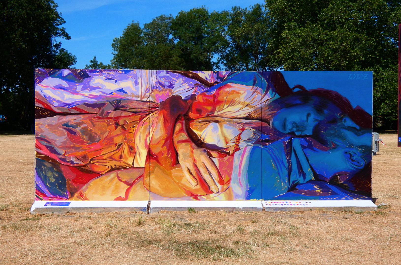 Fresque murale colorée représentant deux personnes allongées ou enlacées, peintes dans des tons vifs de bleu, rouge, orange et violet, installée en plein air dans le cadre du festival Plein Champ dans la ville du Mans.