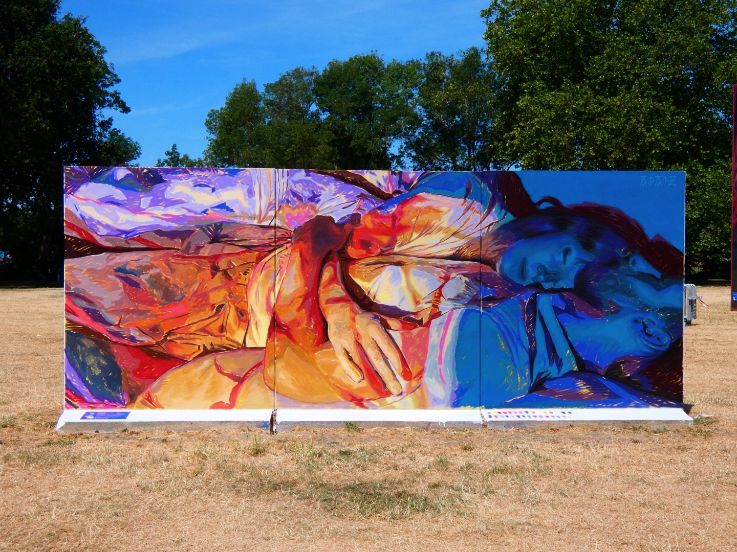 Fresque murale colorée représentant deux personnes allongées ou enlacées, peintes dans des tons vifs de bleu, rouge, orange et violet, installée en plein air dans le cadre du festival Plein Champ dans la ville du Mans.