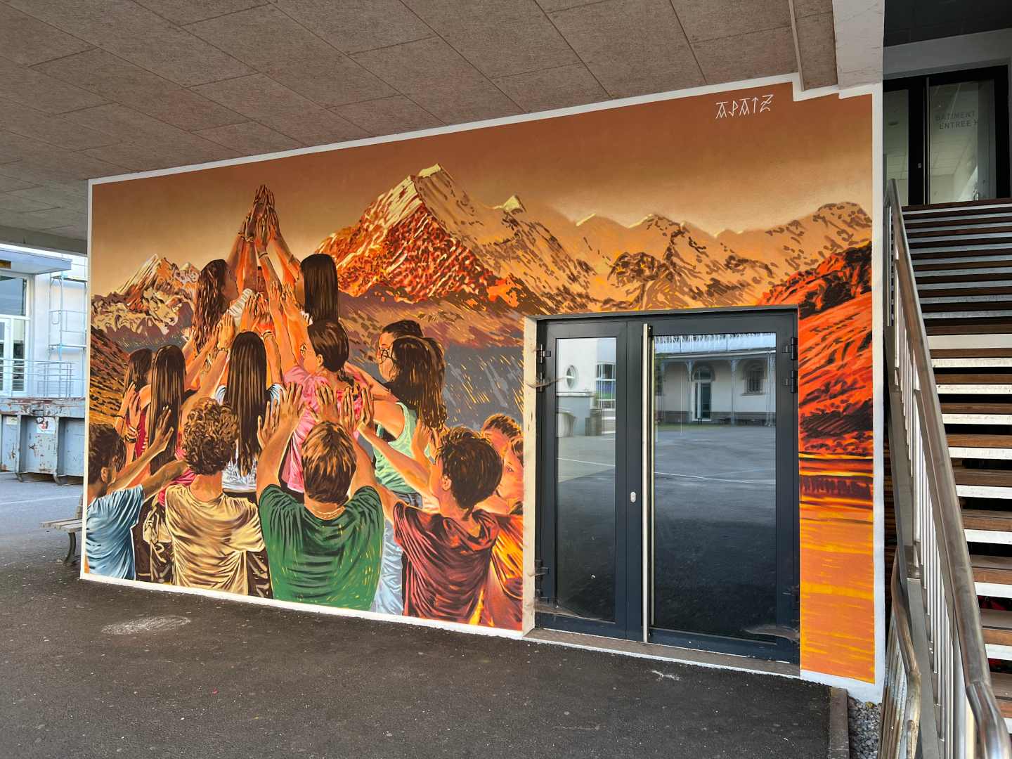 Fresque murale réalisée par APAIZ, représentant un groupe de personnes levant les mains devant un paysage alpin