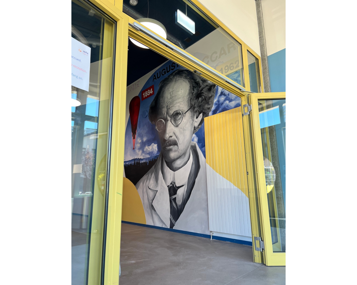 Fresque murale d’Auguste Piccard, pionnier de l’exploration de la stratosphère, entouré de son ballon, de nuages et de formes géométriques.