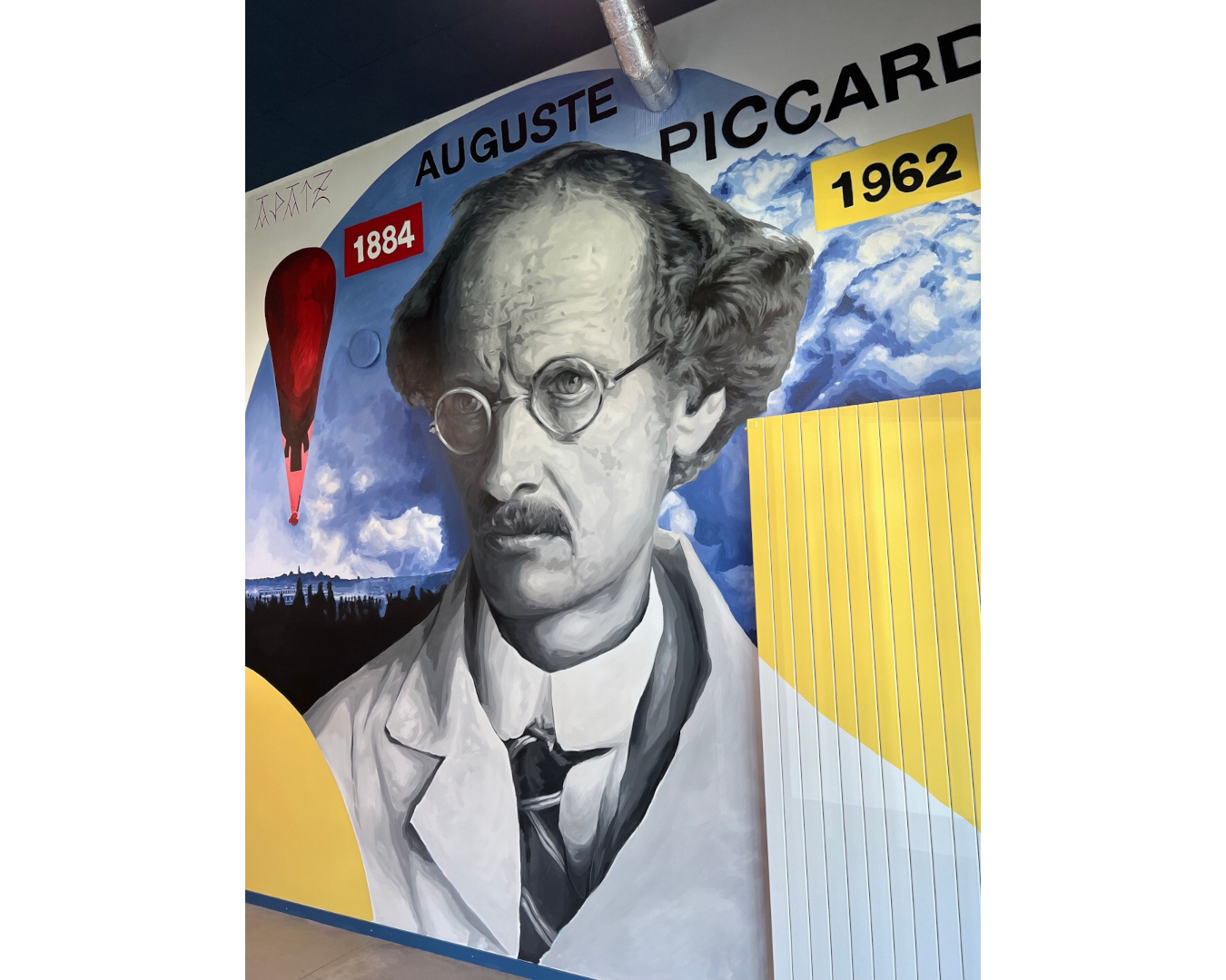 Fresque murale d’Auguste Piccard, pionnier de l’exploration de la stratosphère, entouré de son ballon, de nuages et de formes géométriques.